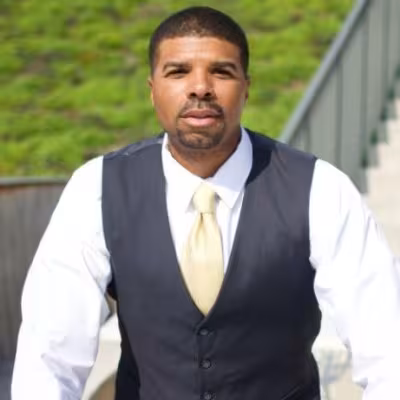 GRCC alumnus Ruben Watson is dressed in business attire posing outside.