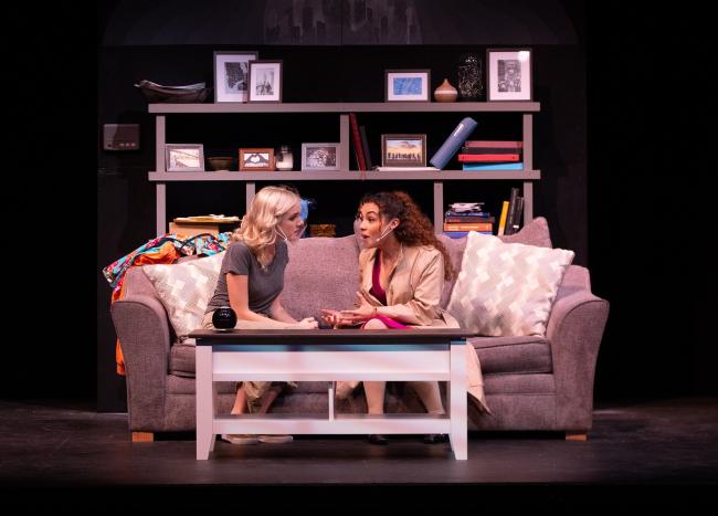 Performers rehearsing a scene on a set with a sofa and bookshelf.