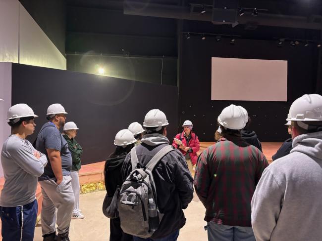 A group of students listen to an architect during a construction site tour.