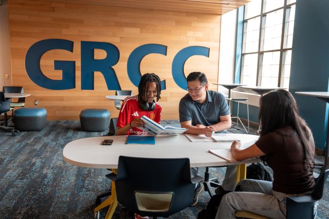 Three people study at a desk together in front of a GRCC wall sign.
