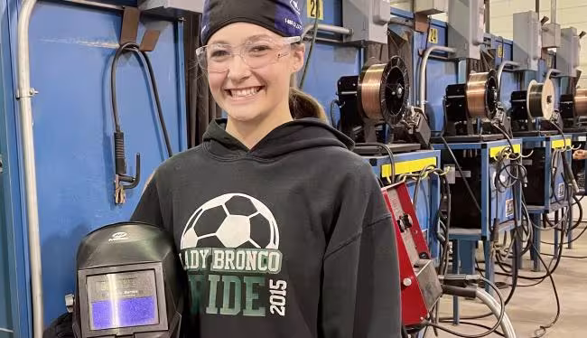 Andrea Ziebarth in the shop holding a welder's mask.