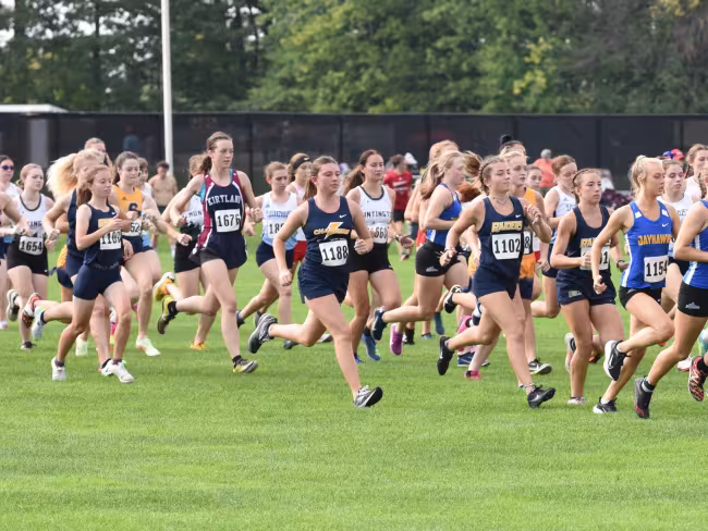 Women cross country team members racing in a large group.