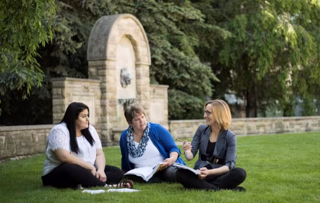 Students sitting ont he grass near the iconic lion statue.
