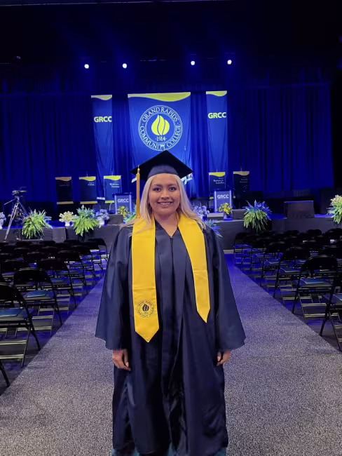 Yesenia is in her cap and gown in front of the stage at commencement.
