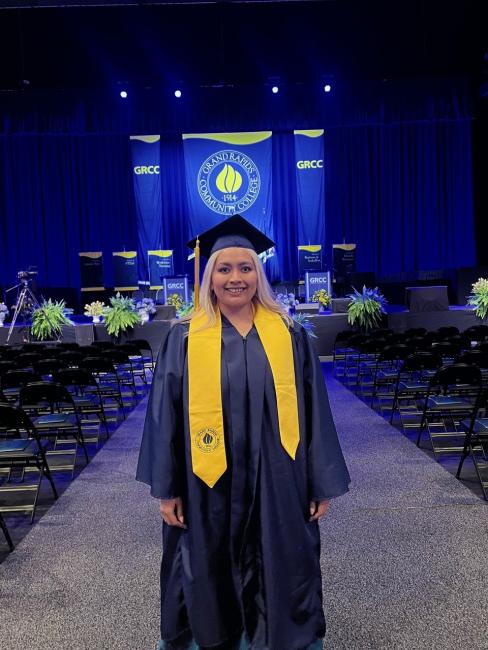 Yesenia is in her cap and gown in front of the stage at commencement.