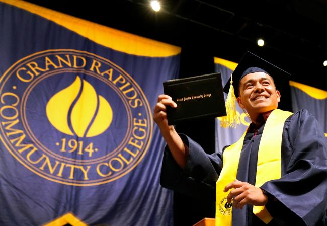A student holding up his diploma case at commencement.