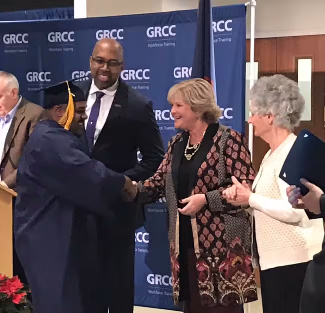 A Job Training graduate shakes Amy Mansfield's hand while Bill Pink and Cynthia Bristol look on.