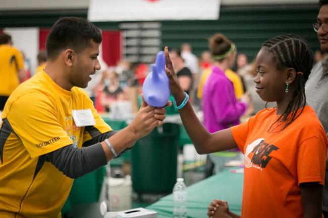 One person holds up an inflated rubber glove to another person.