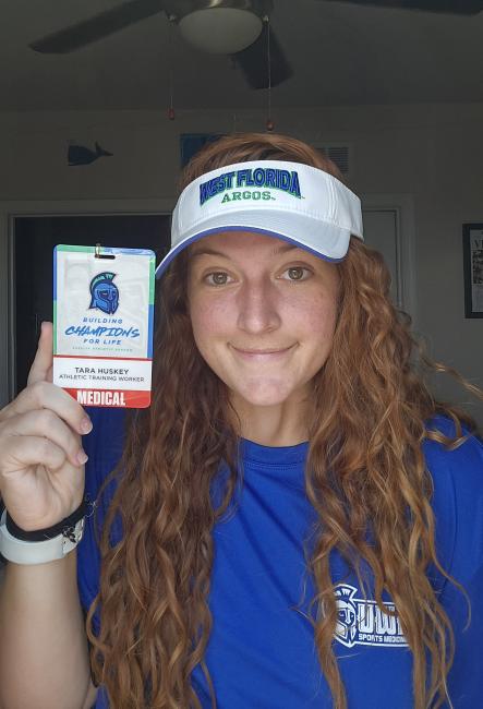 Tara Huskey holds a badge from the University of West Florida that says "Athletic Training Worker"