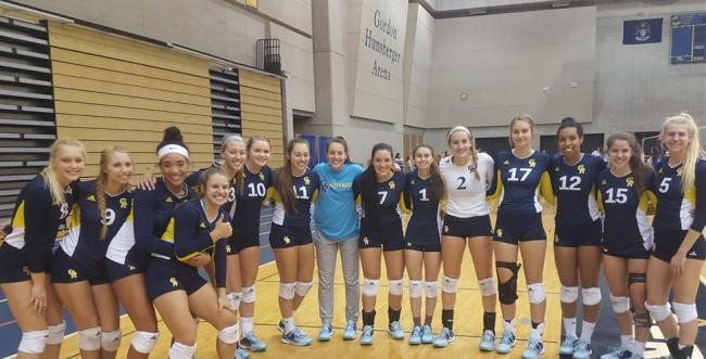 Volleyball team members stand in a row in the fieldhouse with their arms around each other.