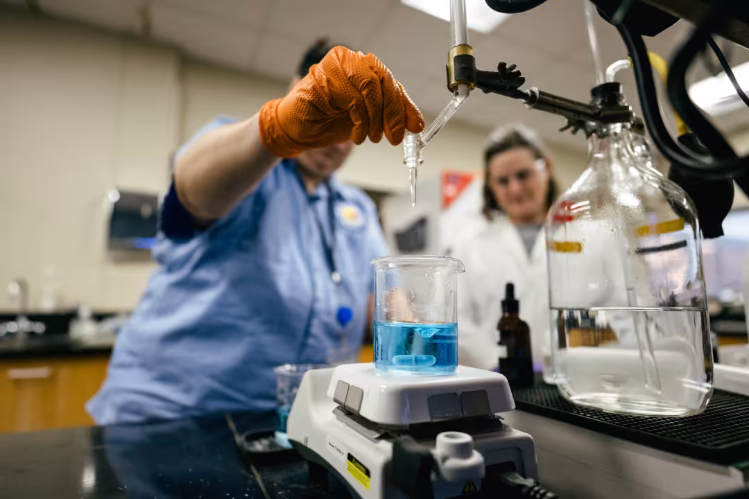 People use lab equipment and beakers to pour a blue liquid.