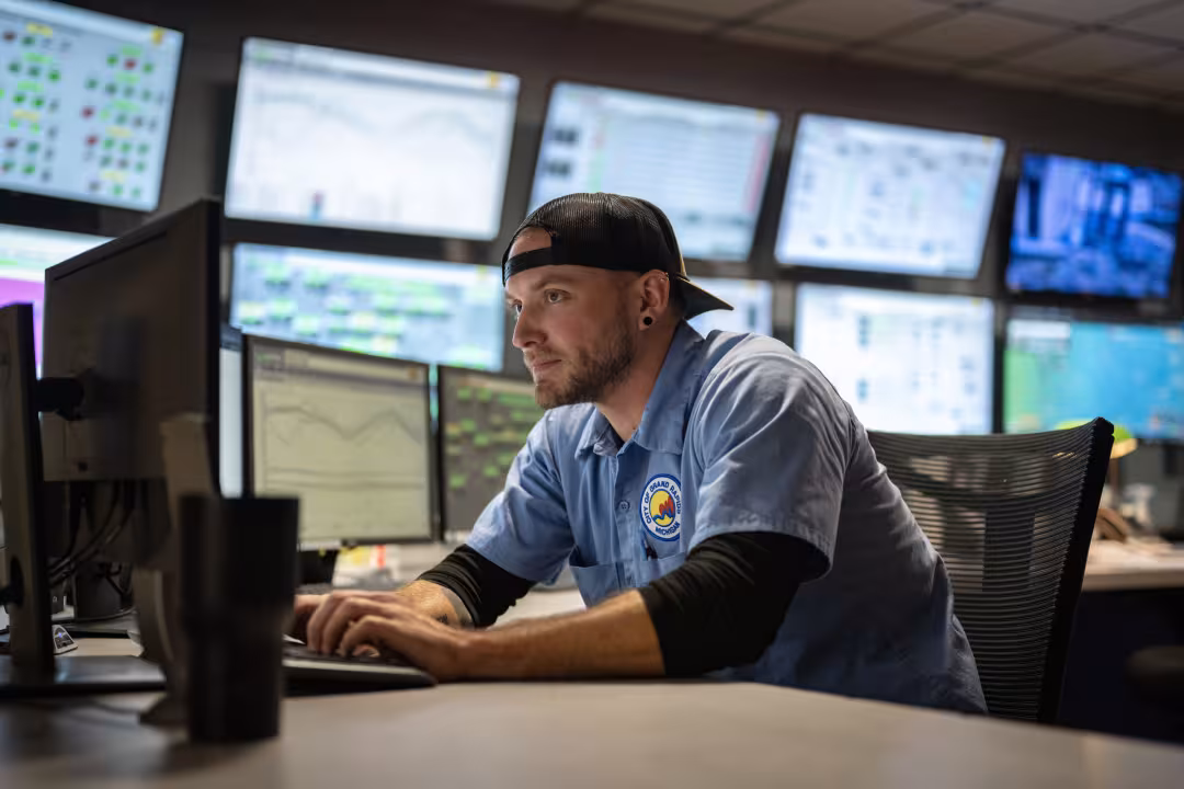 A person wearing a City of Grand Rapids shirt sits at a desk in front of dozens of computer screens.