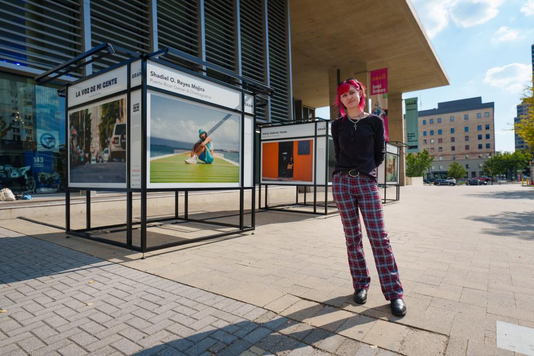 A person stands in front of three welded frames, each holding images and names of artists.