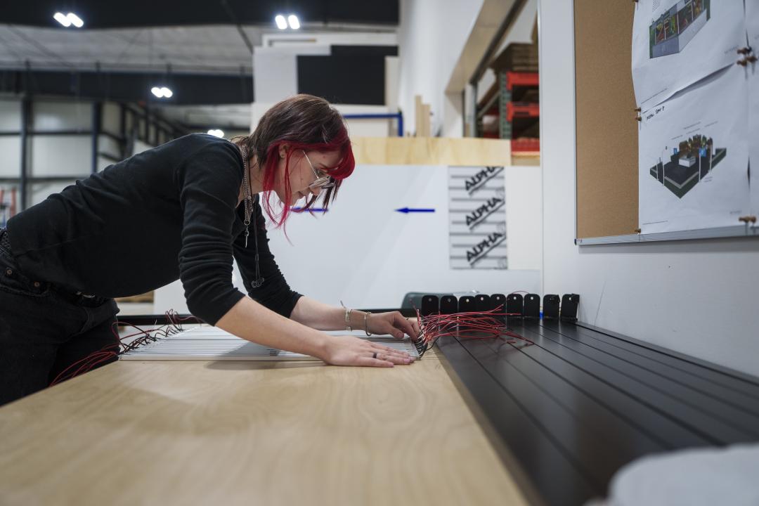 A person works at a large table with rod-like components with wires.