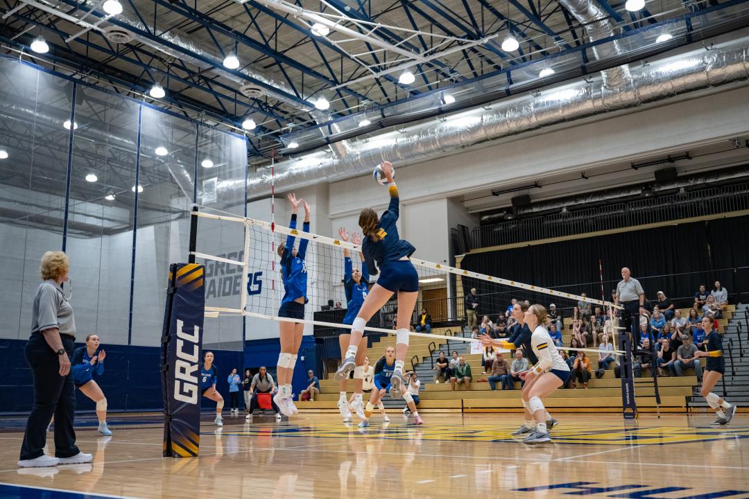 A GRCC volley ball player spikes the ball toward opposing team players.