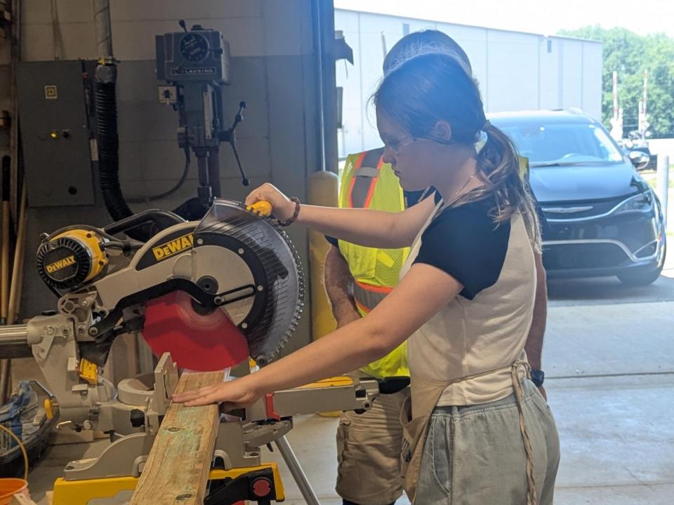 Two people use a saw to cut a board.