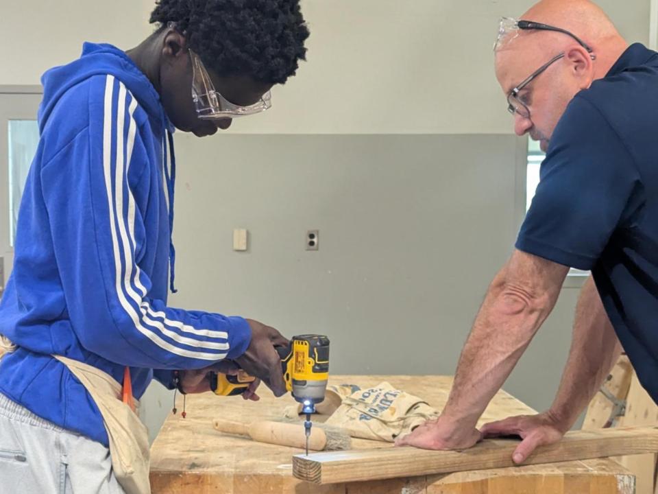 One person uses a drill while another holds a board in place.