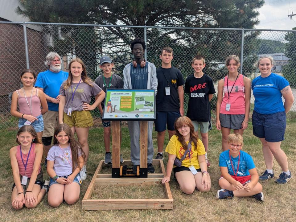 11 campers and instructors pose with a boot brush station and plaque.