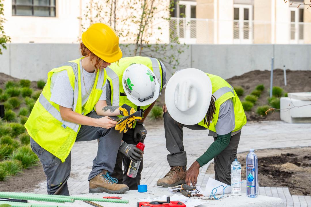 Three people in reflective vests look at documents.