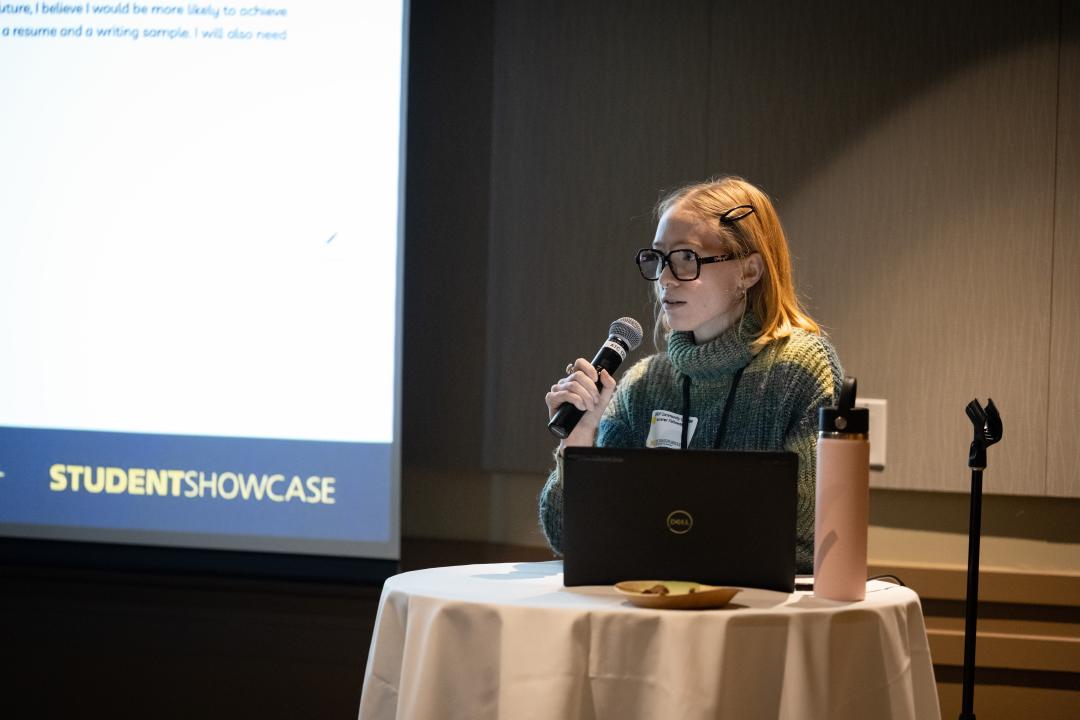 A person speaks into a microphone from a podium during a presentation.