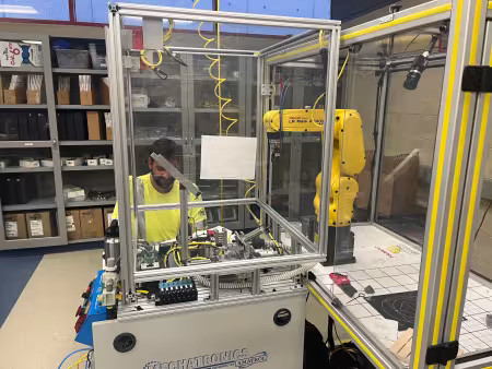 A person sits at a computer near a robotic arm.