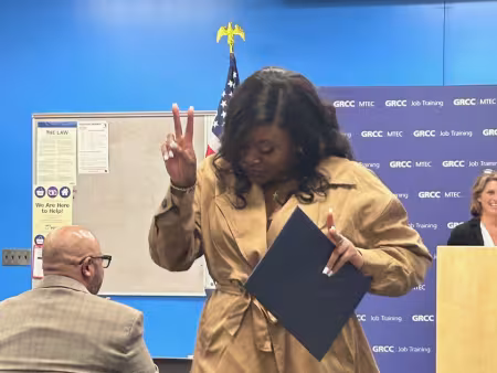 Juané Lancaster holds a diploma and holds up a peace sign.