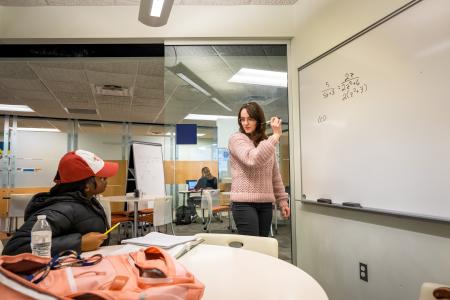 A math tutor writes out a problem on a white board in a study room.