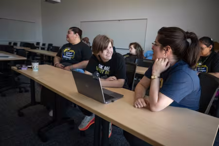 Two students sit at a laptop, talking