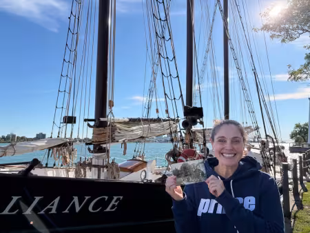 Professor Lynn Prince poses next to the tall ship with a picture of her great-great-grandfather.
