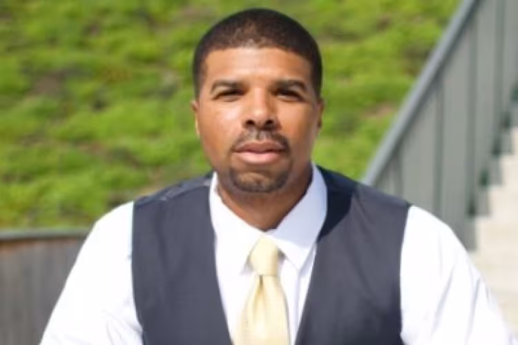 GRCC alumnus Ruben Watson is dressed in business attire posing outside.