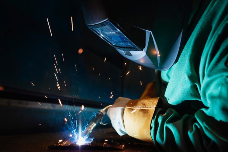 A student wearing welding gear practices welding.
