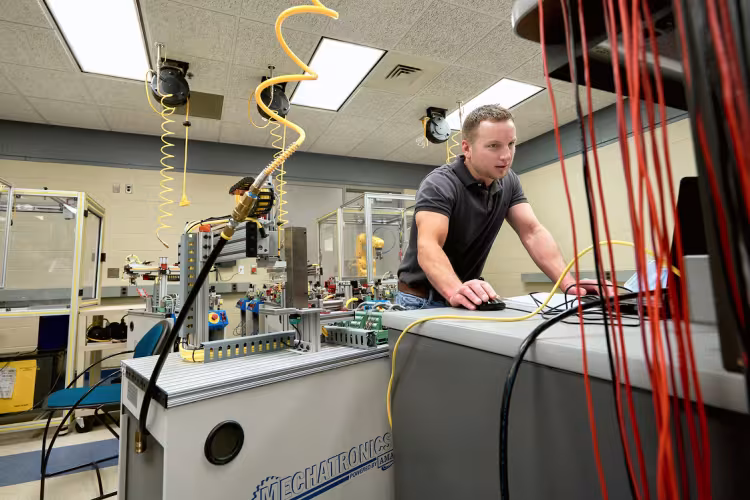 A male student works on the mechatronics line surrounded by equiprment at GRCC.