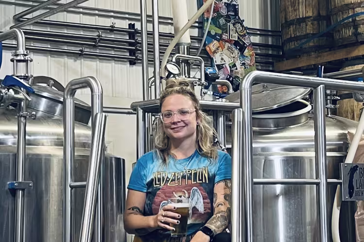 GRCC Alumnus Casey Brunetti poses near brewing equipment with a glass of beer in hand.