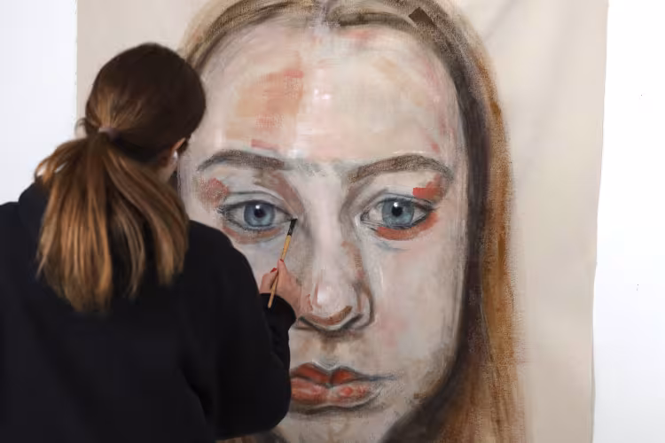 Erin Reinholz paints a face on a large canvas.