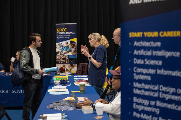 A young male talks with GRCC staff about admissions and academic pathways at an open house.