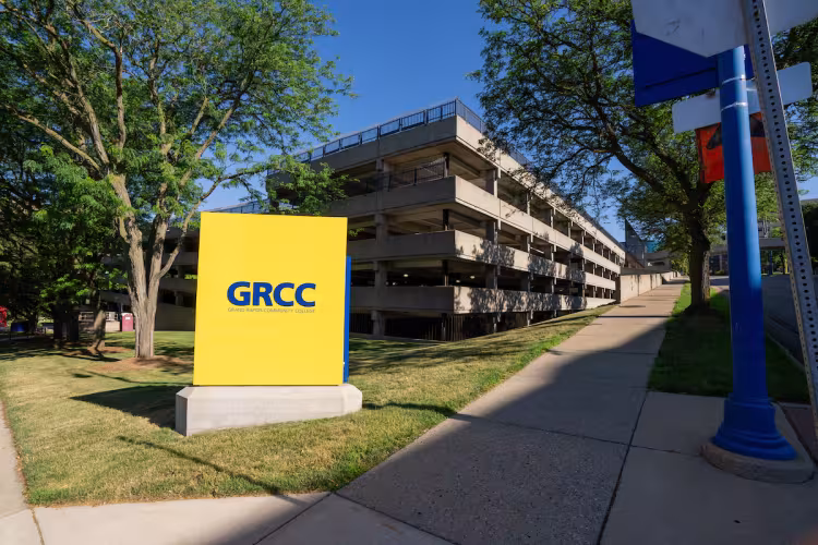 A blue and gold Grand Rapids Community College sign is shown in front of a campus structure.