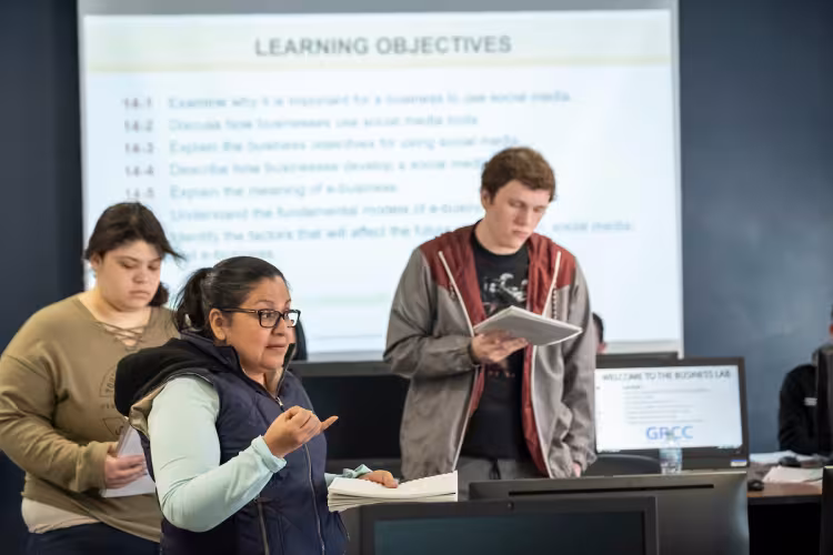 Three students speak at the front of a classroom in GRCC's Intro to Business course.