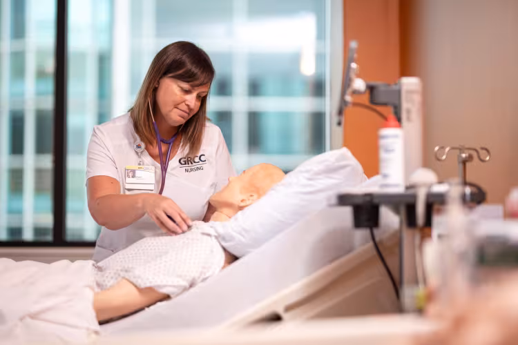 A GRCC nursing student works with a mannequin on a hospital bed.