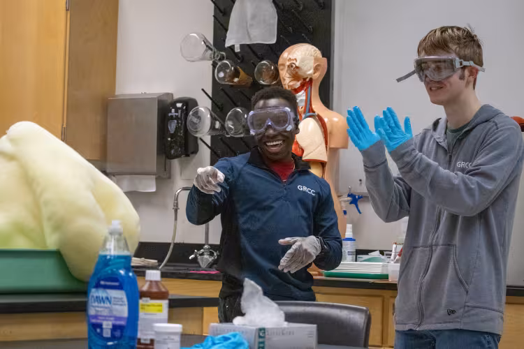 Two people in gloves and goggles cheer as foam spills from a basin.