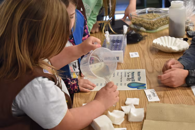 A child pours liquid into a cup at Water Pool-ooza.