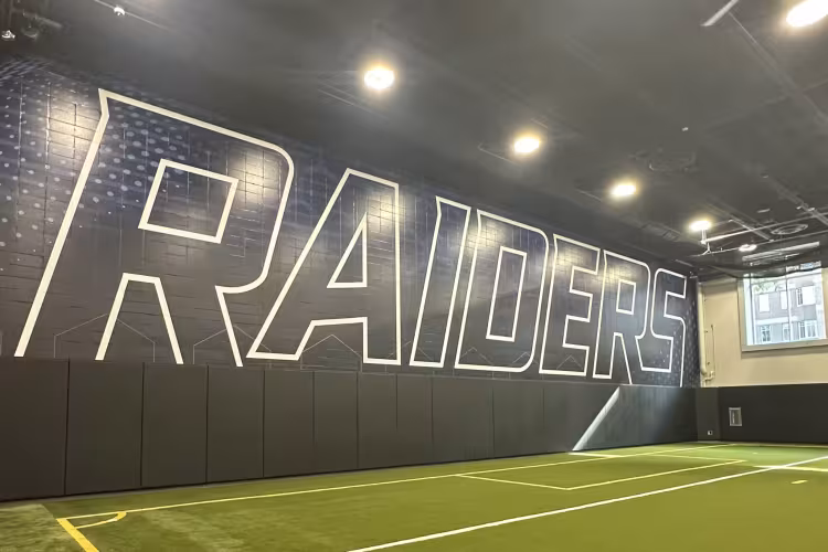 An indoor turf field with the word "Raiders" on the wall