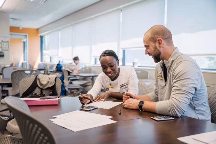 A person wearing a GRCC nursing shirt works with another person at a table.