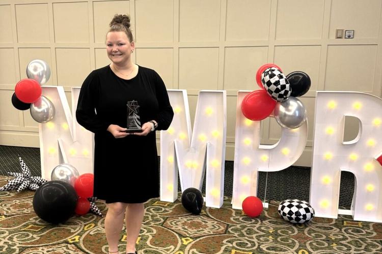 Kailee Potgeter poses with an award in front of balloons and large letters spelling NCMPR.