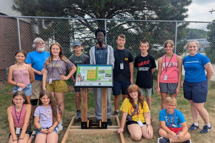 11 campers and instructors pose with a boot brush station and plaque.