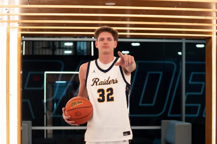 GRCC athlete Jakob Chapman stands confidently holding a basketball and pointing at the camera