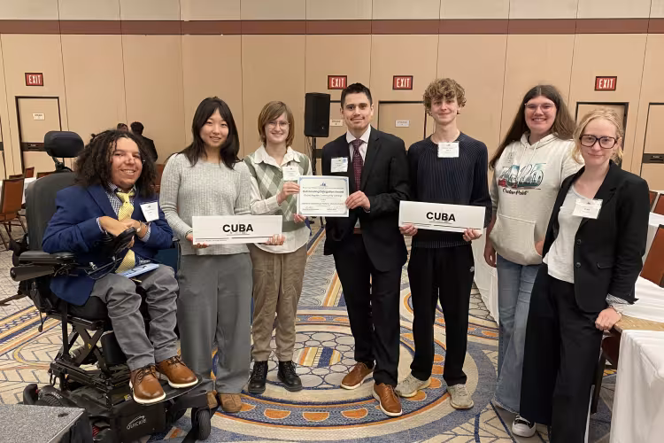 Seven students pose, some holding an award and paper signs reading "Cuba."