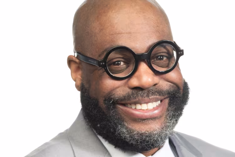 Maurice Baker in a gray suit and glasses.
