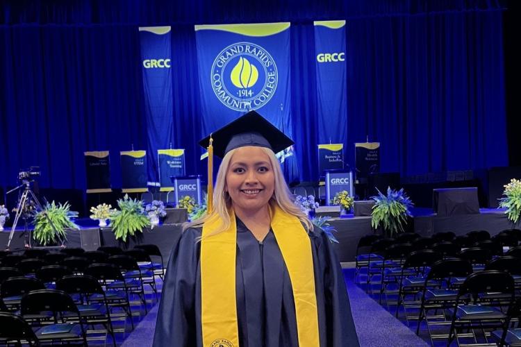 Yesenia is in her cap and gown in front of the stage at commencement.