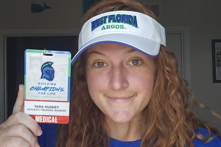Tara Huskey holds a badge from the University of West Florida that says "Athletic Training Worker"