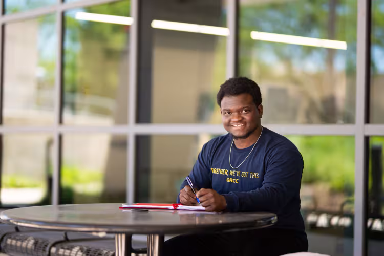 GRCC student sits at an outside table with a notebook.
